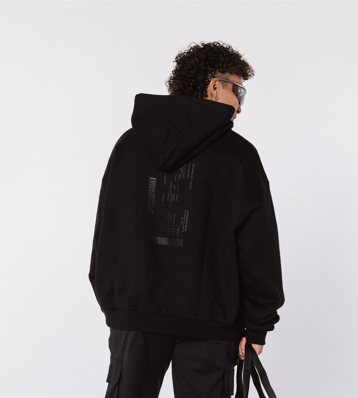 [Color: Black Out] Model wearing the LA Hoodie with subtle text detail on the back, paired with black cargo pants and futuristic wraparound sunglasses.